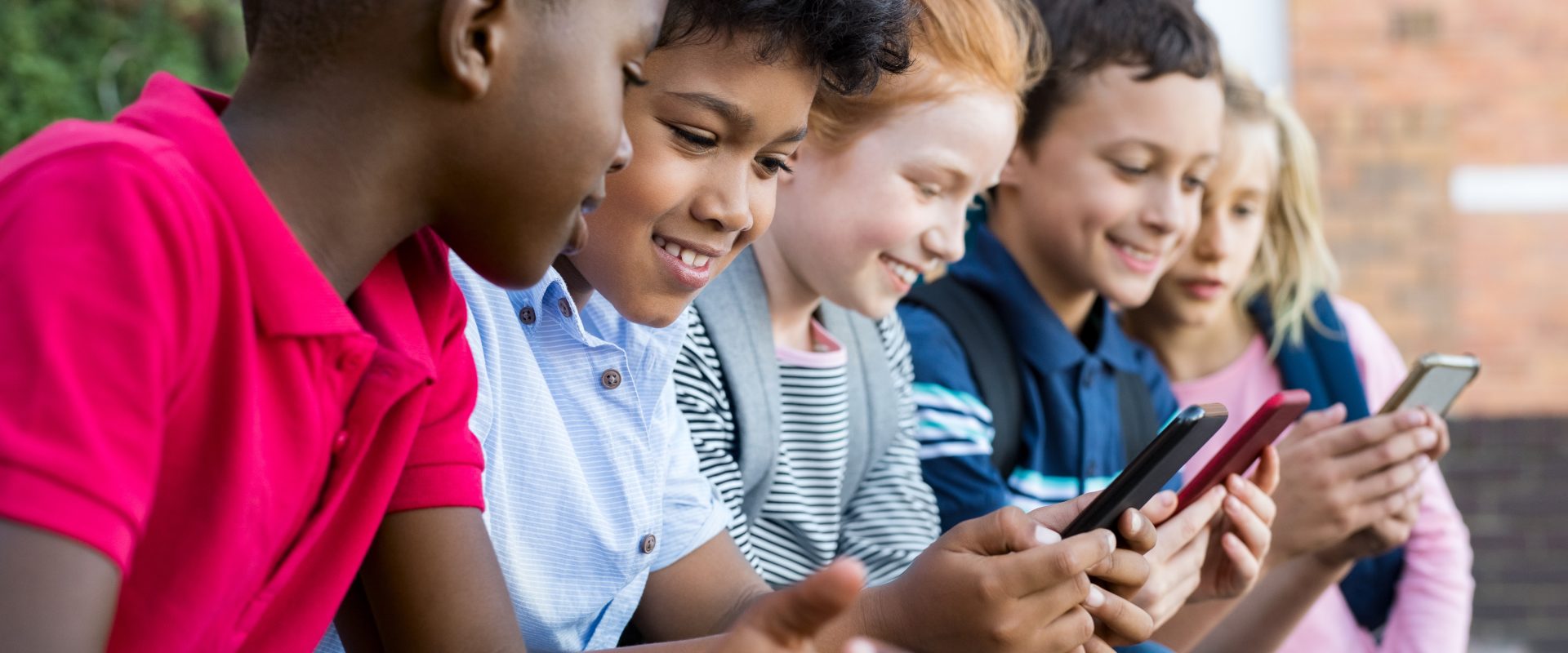 Children sitting outdoors, looking at mobile phones.